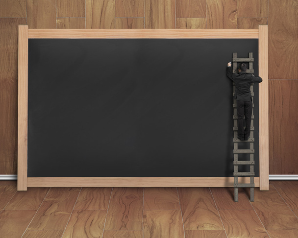 businessman climbing ladder drawing on black blank chalkboard - Photo, Image