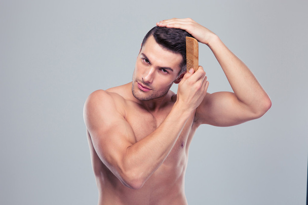 Handsome young man combing his hair - 写真・画像