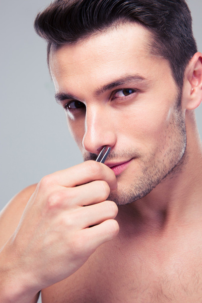 Man plucking nose hair with tweezers - Photo, image