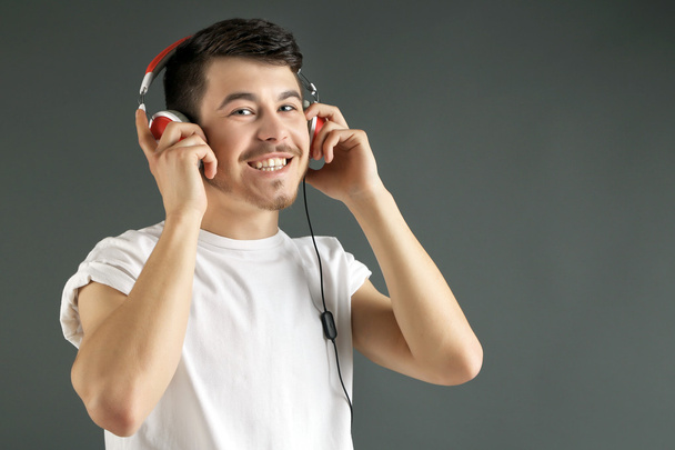 Handsome young man listening to music on grey background - Photo, Image