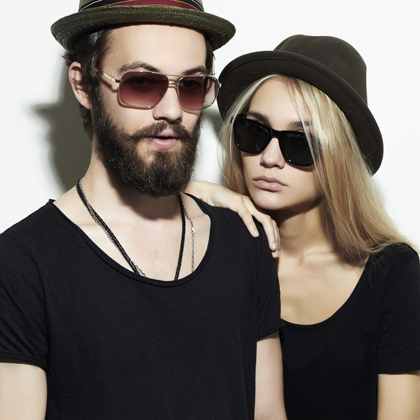 όμορφη ευτυχισμένο ζευγάρι με το καπέλο που φορούν μοντέρνα γυαλιά μαζί. hipster αγόρι και κορίτσι. γενειοφόρος νέος και ξανθιά σε γυαλιά ηλίου - Φωτογραφία, εικόνα