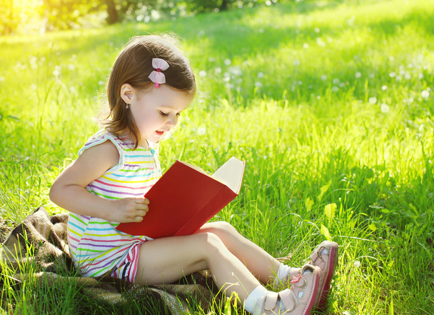 Child reading a book on the grass in sunny summer day - Foto, afbeelding