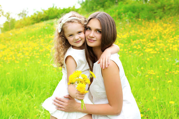 Sunny portrait of mother and daughter together with yellow dande - Photo, image
