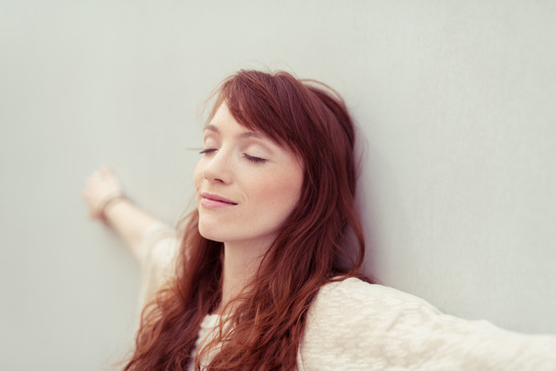 Serene young woman relaxing against a wall - 写真・画像