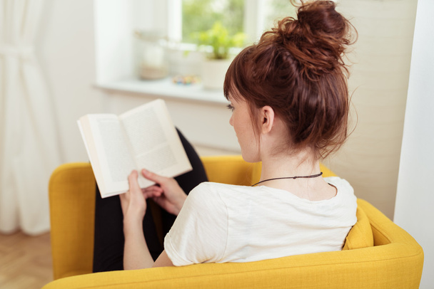 Young Woman Reading a Book While Sitting on Chair - Foto, imagen