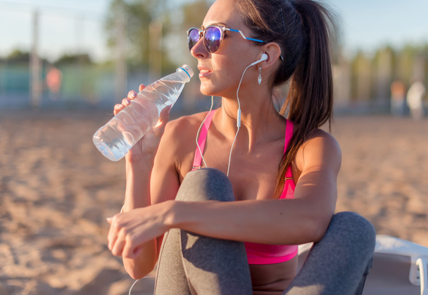 Beautiful fitness athlete woman drinking water after work out exercising on summer in beach outdoor portrait. - Photo, Image