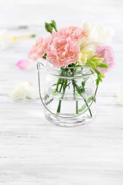 Beautiful spring flowers in glass bottle on wooden background - Foto, imagen