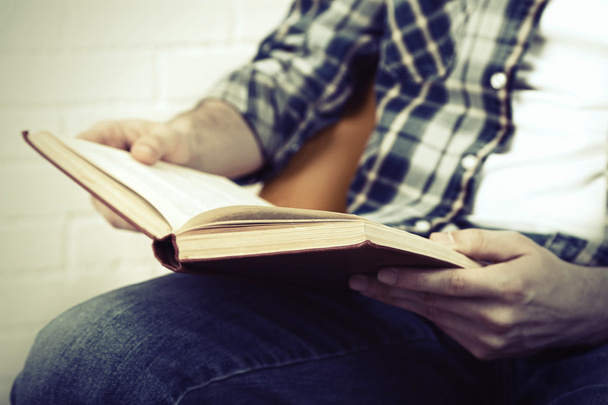 Nuori mies lukemassa kirjaa, lähikuva, valoisalla taustalla
 - Valokuva, kuva