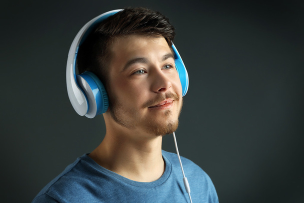 pohledný mladý muž poslouchat hudbu na šedém pozadí - Fotografie, Obrázek