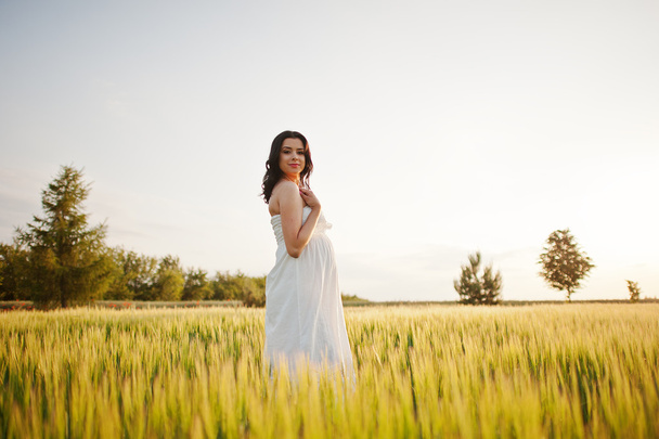 Pregnant gorgeous brunette woman on the field with wheat and pop - Foto, imagen