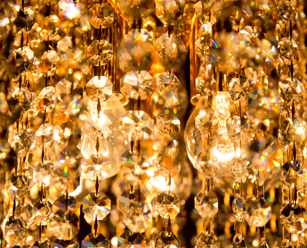 una lámpara de araña de cristal brilla con luz dorada
 - Foto, Imagen
