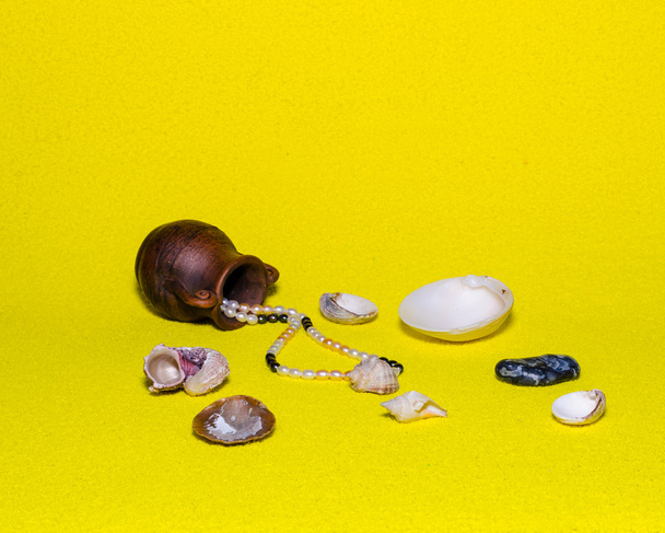 cuentas de perlas, ánfora antigua y concha de mar sobre un fondo amarillo
 - Foto, imagen
