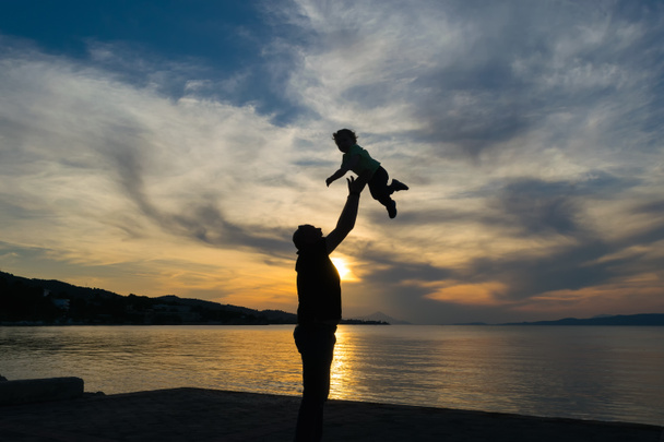 Silhouette d'un père et de son fils contre le coucher du soleil avec un ciel dramatique
. - Photo, image