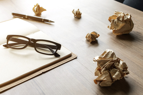 τσαλακωμένο χαρτί μπάλες με γυαλιά και σημειωματάριο στο ξύλινο γραφείο - Φωτογραφία, εικόνα