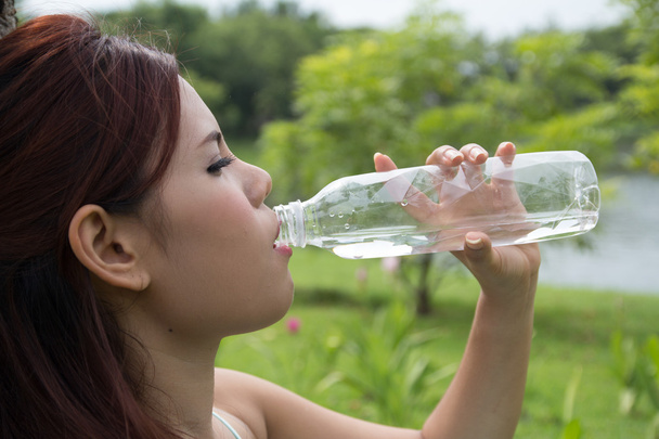 Young woman drinking water at park - Photo, Image