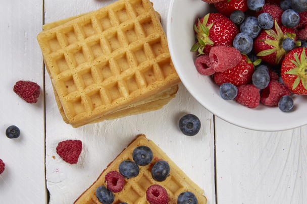Berries on a waffle and in a bowl on a white wooden table - Photo, image