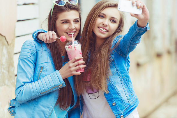 Хипстерские девушки делают селфи в городском контексте - Концепция дружбы и веселья с новыми тенденциями и технологиями - Лучшие друзья увековечивают момент с помощью современного смартфона
 - Фото, изображение