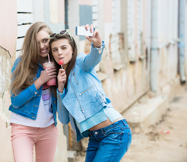 Hipster girlfriends taking a selfie in urban city context - Concept of friendship and fun with new trends and technology - Best friends eternalizing the moment with modern smartphone - Photo, Image