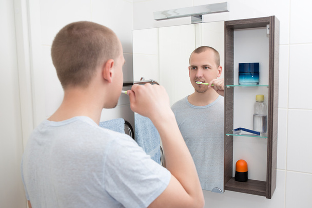 Мужчина чистит зубы и смотрит на зеркало в ванной комнате
 - Фото, изображение