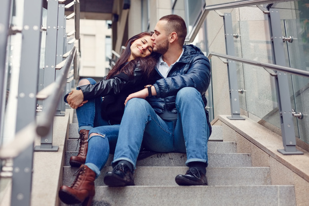 Beautiful young couple in love on a date outdoors on modern urban background. Smiling and hugging. Bearded handsome man and brunette pretty woman in casual dress. - Фото, изображение
