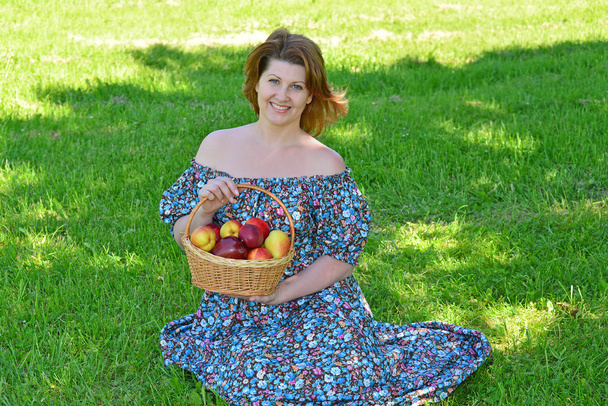 adult woman with a basket of fruit in the park - Фото, изображение