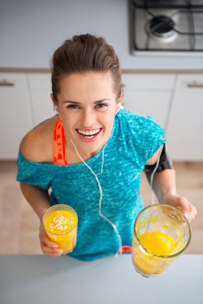 Athletic smiling woman holding freshly-made smoothie in kitchen - 写真・画像