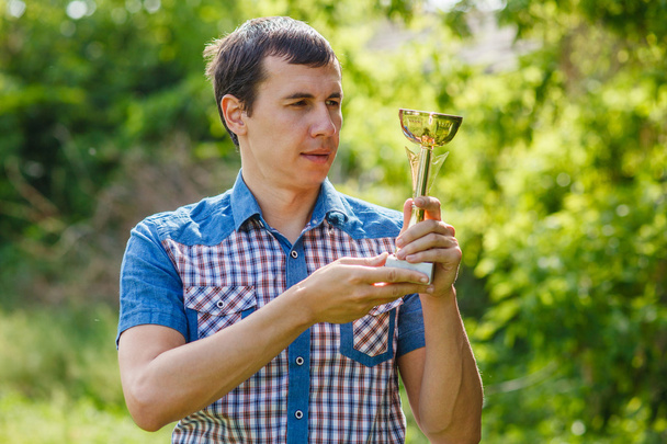 man met een sport cup op de straat overwinning tegen de groene - Foto, afbeelding