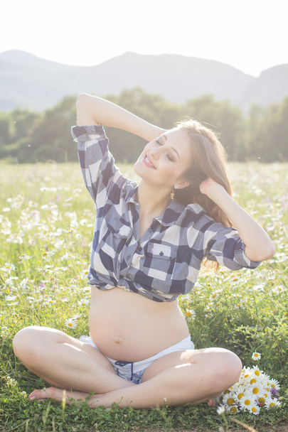 Mujer embarazada sentada en la naturaleza detrás de las luces del atardecer
 - Foto, Imagen