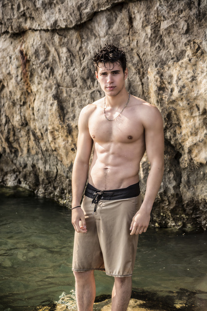 Young shirtless athletic man standing in water by ocean shore - Photo, Image