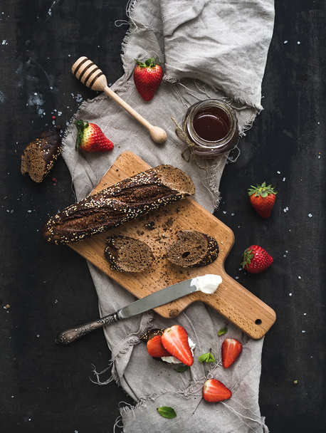 Breakfast set. Black baguette toasts with fresh strawberries, honey and mascarpone cheese on dark grunge table surface - Фото, изображение