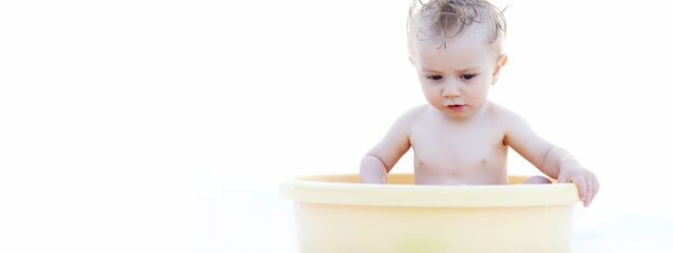 Baby Sitting in a Yellow Bath Basin Against White - Foto, imagen