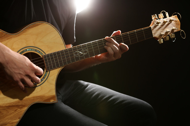 Young man playing on acoustic guitar on dark background - Фото, изображение