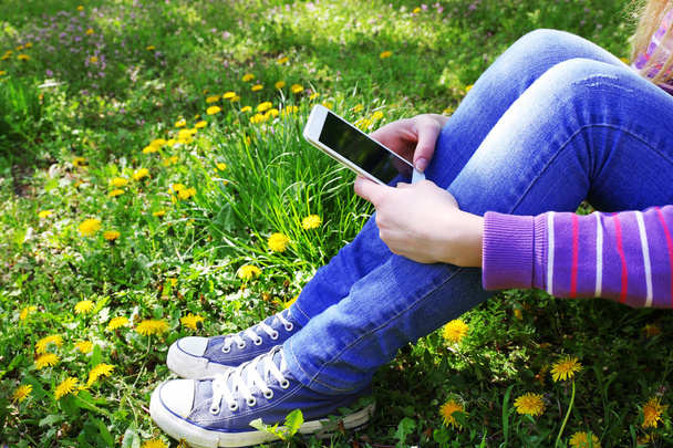 Young woman with mobile phone sitting on green grass outdoors - Fotoğraf, Görsel