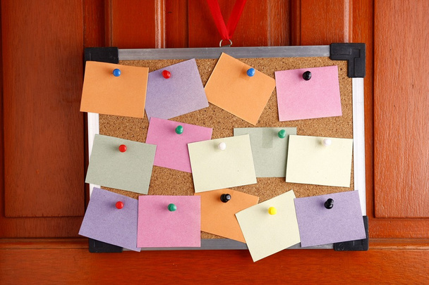 Cork board with colorful papers and push pins hanging by a door - Photo, Image