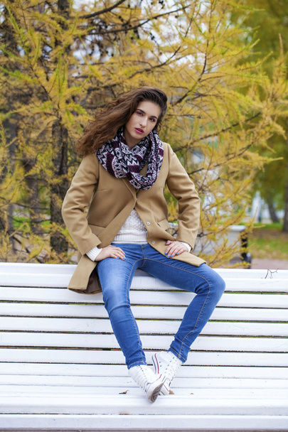 Young beautiful girl in a beige coat sitting on a bench in the s - Fotoğraf, Görsel