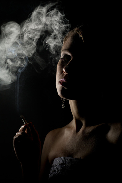 Beautiful woman with a cigarette in the dark - Фото, изображение