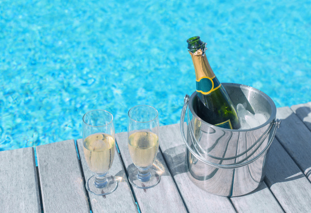 Cold champagne bottle in ice bucket and two glasses of champagne on the deck by the swimming pool - Fotoğraf, Görsel