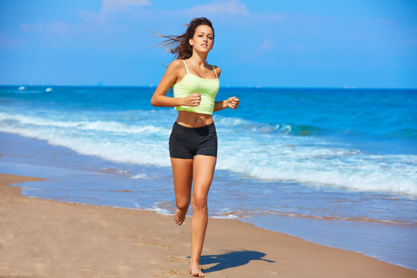 όμορφη μελαχρινή κοπέλα που τρέχει σε μια παραλία το καλοκαίρι - Φωτογραφία, εικόνα