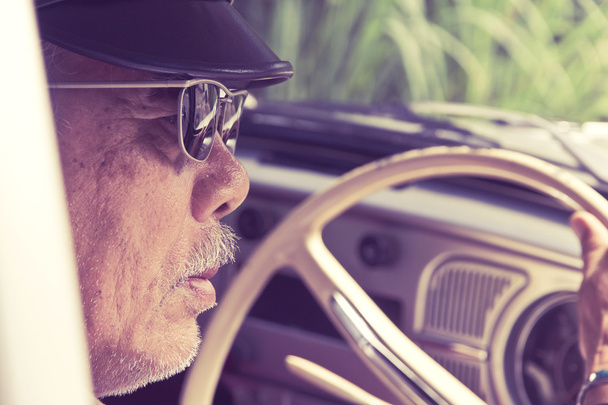 Vanhempi silmälasipäinen mies ajaa autoa
 - Valokuva, kuva