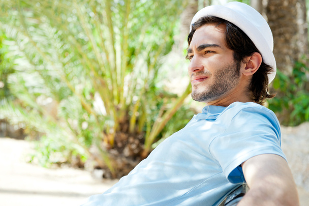 Portrait of a handsome young man sitting in the sun on bench at - 写真・画像