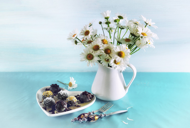 Still life with chocolates and a bouquet of daisies on a blue ba - 写真・画像