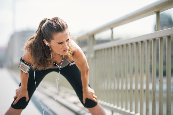 Woman jogger stretching on bridge while listening to music - Foto, Imagem