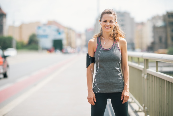 Smiling woman jogger standing still on bridge - Photo, image