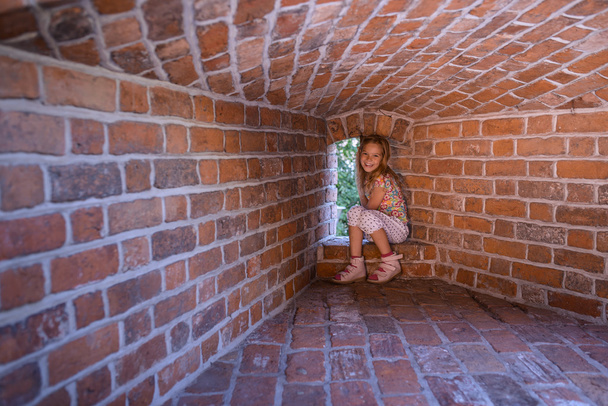 Маленька дівчинка сидить на стіні фортеці
 - Фото, зображення