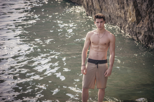 Young shirtless athletic man standing on rock by sea - Foto, Bild
