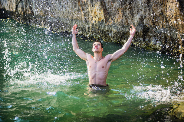 Handsome young athletic man in the sea, splashing water up - Photo, Image