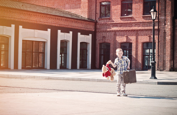 little kid is holding the suitcase and teddy bear toy and walkin - Fotografie, Obrázek