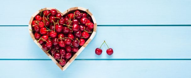 Cherries in a heart box on blue wooden table top view - Valokuva, kuva