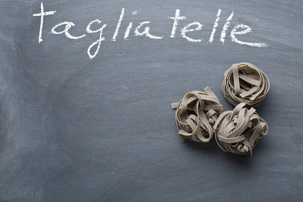 black tagliatelle pasta on chalkboard - Foto, Imagen
