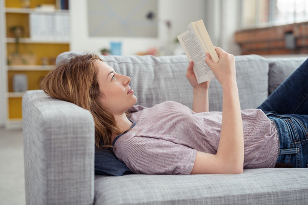 若い女性本のソファの上でリラックス - 写真・画像